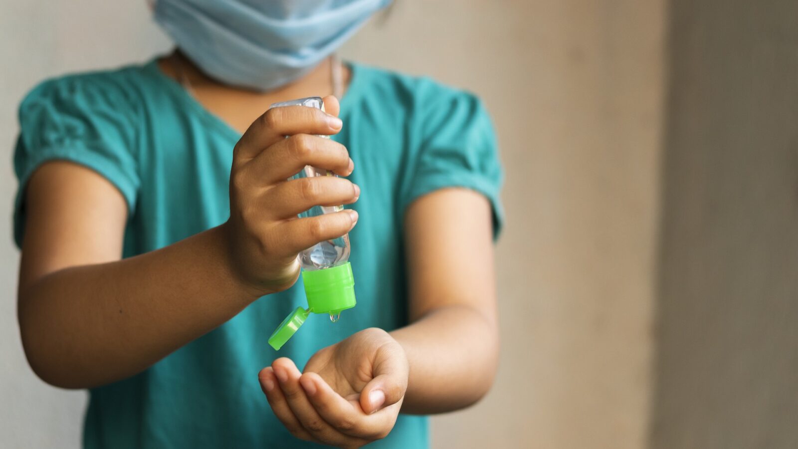 Image of child in a mask using hand sanitiser